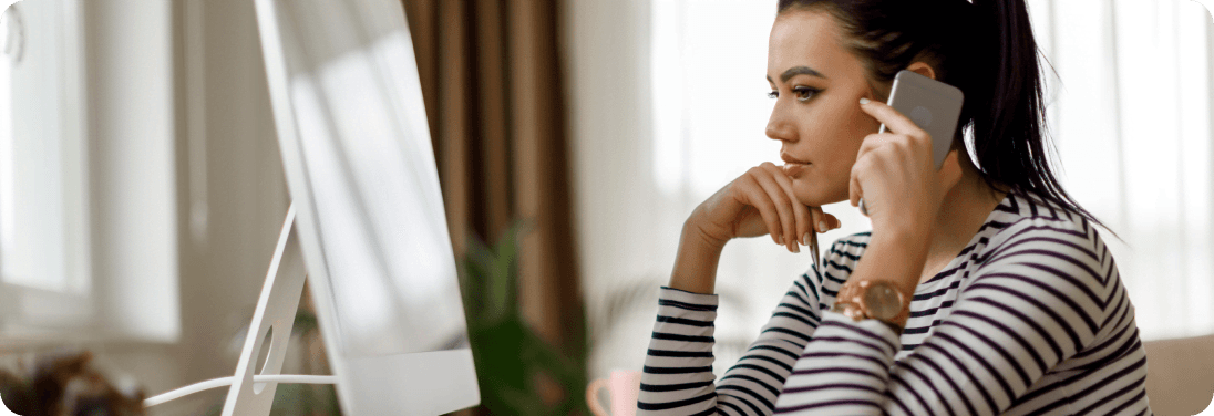 Woman on cell phone looking at computer moniter