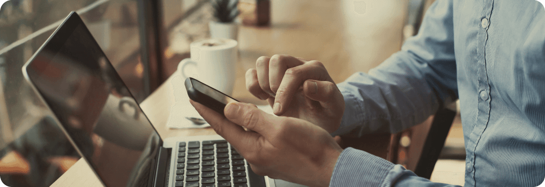 Man holding cell phone sitting infront of laptop at coffee shop