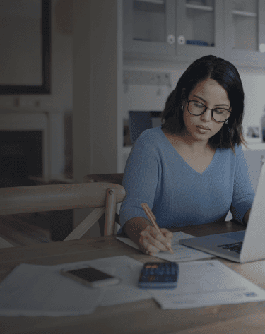 The girl is sitting and working with a pen.