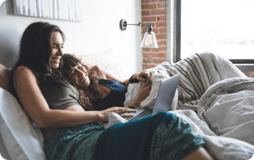 Two women sitting in bed looking at laptop