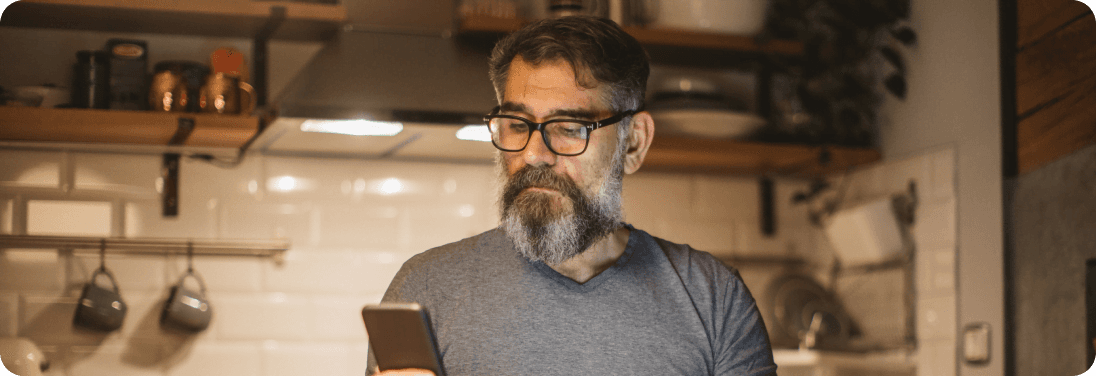 Man with glasses standing in kitchen looking at cell phone