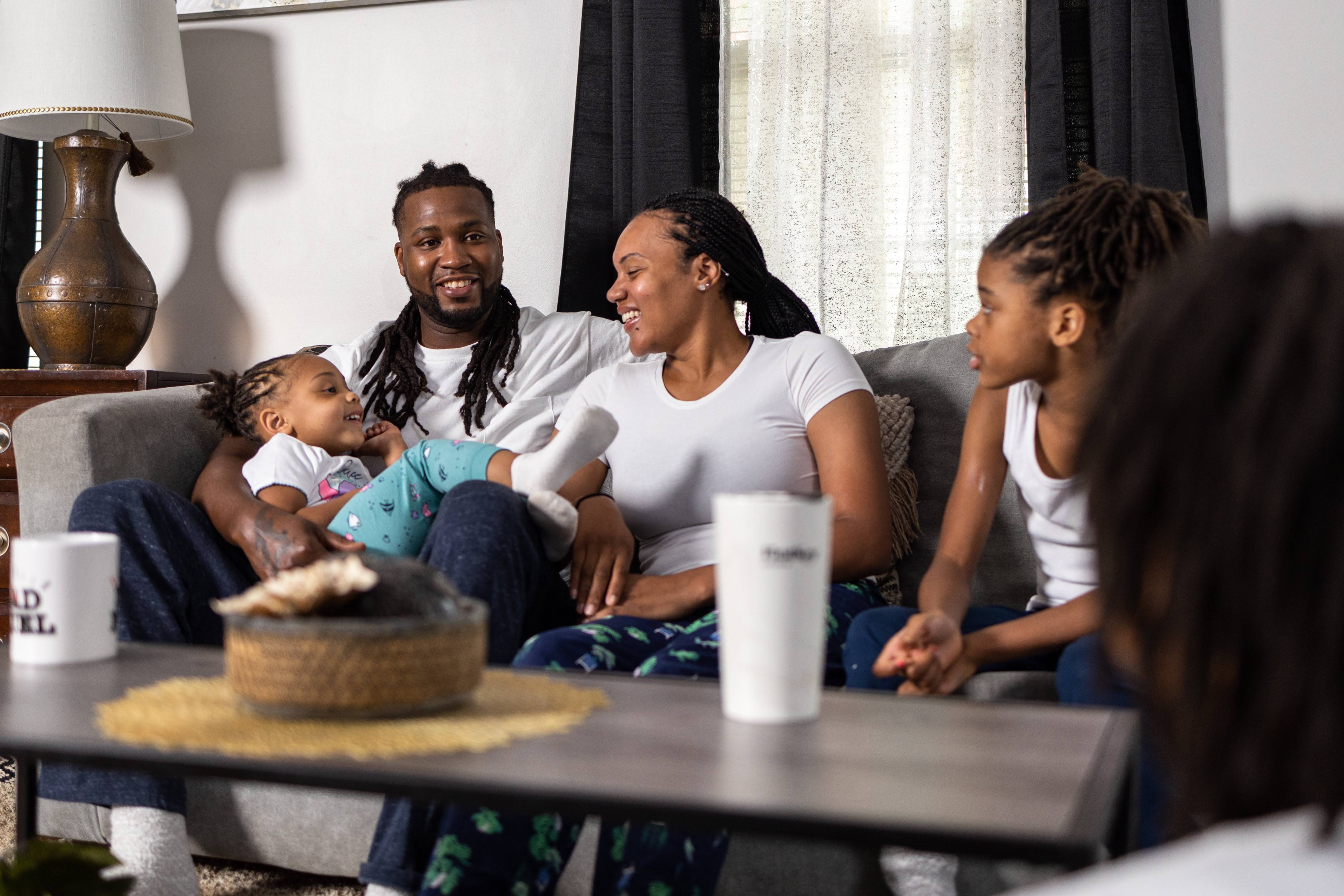 A happy couple is sitting on the sofa with two girls.